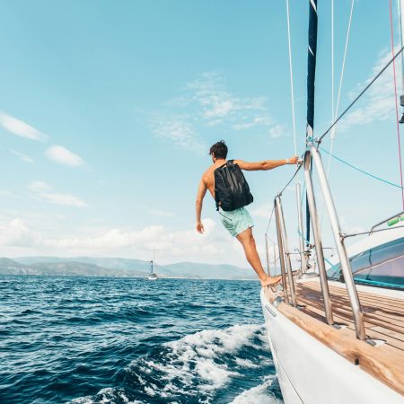 Man sailing in vibrant Greek waters, depicting freedom and adventure under clear skies.